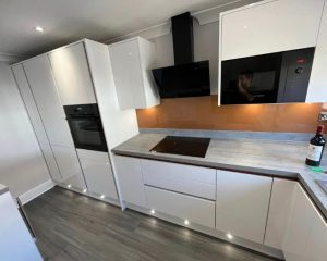 A new kitchen design featuring white cabinets and cupboards, integrated cooker and hob, grey countertops and grey laminate flooring.