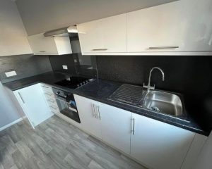 A new kitchen that has been installed at a property in Southampton. Featuring white cabinets and cupboards, black countertops, grey vinyl flooring and integrated cooker and hob.