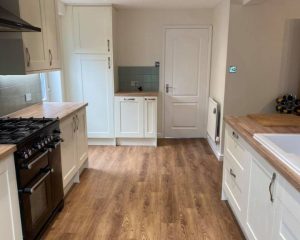 A luxury kitchen that has been fitted in Southampton featuring wooden laminate flooring, wooden worktops, white cabinets and cupboards, green wall tiling and oven with hob.