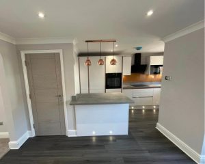 A modern kitchen that has been fitted at a Southampton property that features grey woodn flooring, white kitchen cabinets and cupboards, orange tiled walls and integrated oven and hob.