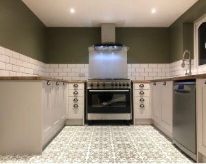 A new kitchen that has been installed in a Southampton property featuring a patterned tile floor, white cabinets, white wall tiling, wooden countertops and an oven with extractor fan.