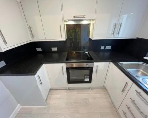 A kitchen that has been installed in Southampton featuring white vinyl flooring, white cabinets and cupboards, black wall tiling and black countertops.