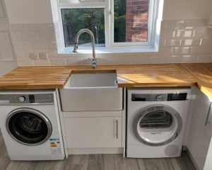 A new residential kitchen fitted in Southampton featuring wooden countertops, grey laminate flooring, a new butler sink, white tiled walls and white kitchen cupboards.