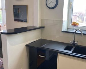 A new kitchen installation featuring white tiled walls, white cabinets, black ceramic countertops and a black composite sink.