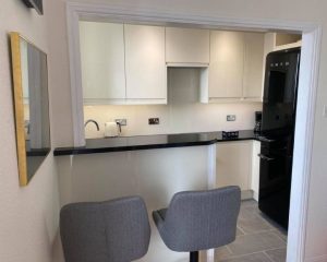 A new residential kitchen installation that features white cabinets and cupboards, a black SMEG fridge, black countertops, a grey tiled floor and white wall tiles.