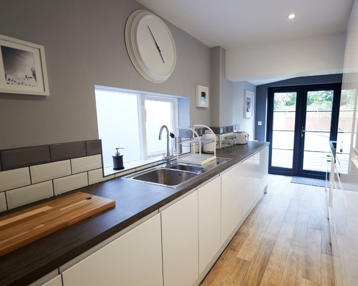 A kitchen that has been recently refurbished with new wooden flooring, white wall tiling and grey painted walls.