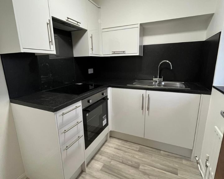 A new kitchen installation featuring white cabinets and cupboards, black wall tiling, black countertops and integrated cooker with extractor fan.