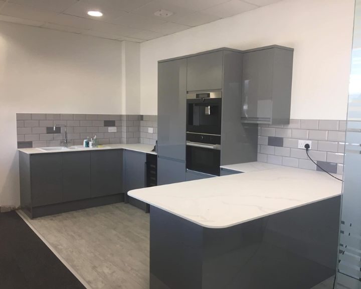 A new commercial kitchen that has been installed in Southampton featuring grey wall tiles, grey cupboards and cabinets, white marble countertops and wooden vinyl flooring.